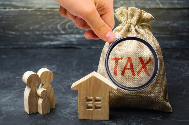 A hand examines a bag of wood labeled with the word “tax,” hinting at concerns about the Michigan estate tax.